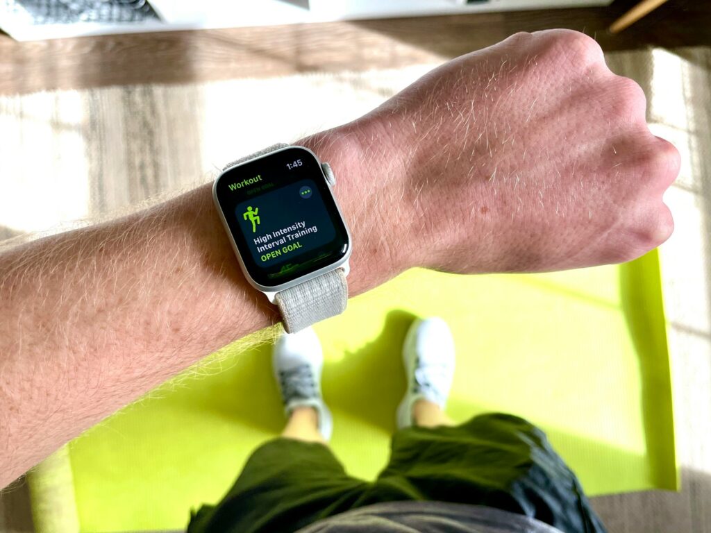 A silver aluminium Apple Watch with a white sport band resting on a surface, screen facing up