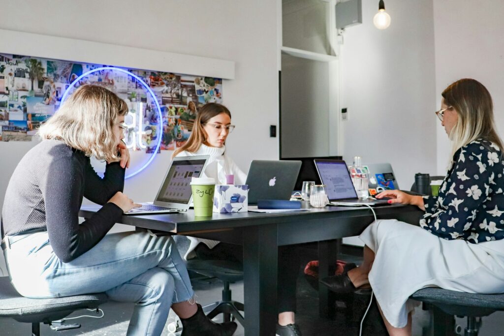 Three software professionals sitting at a table working together on laptops in an office